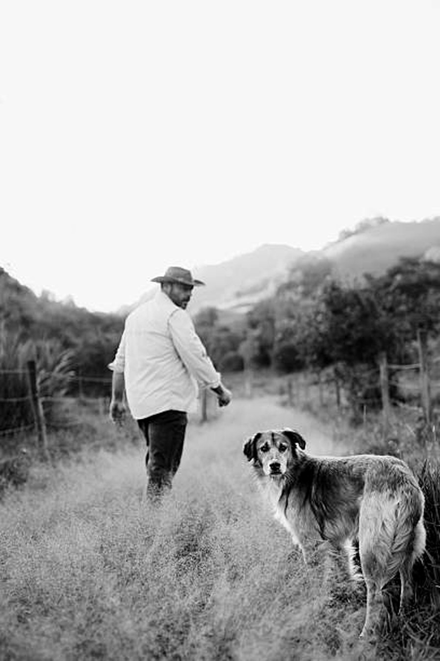 A farmer walking a grassy path with his dog